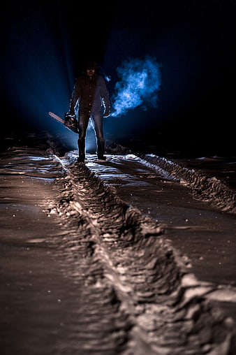 Man with chainsaw in dark snowy forest at night