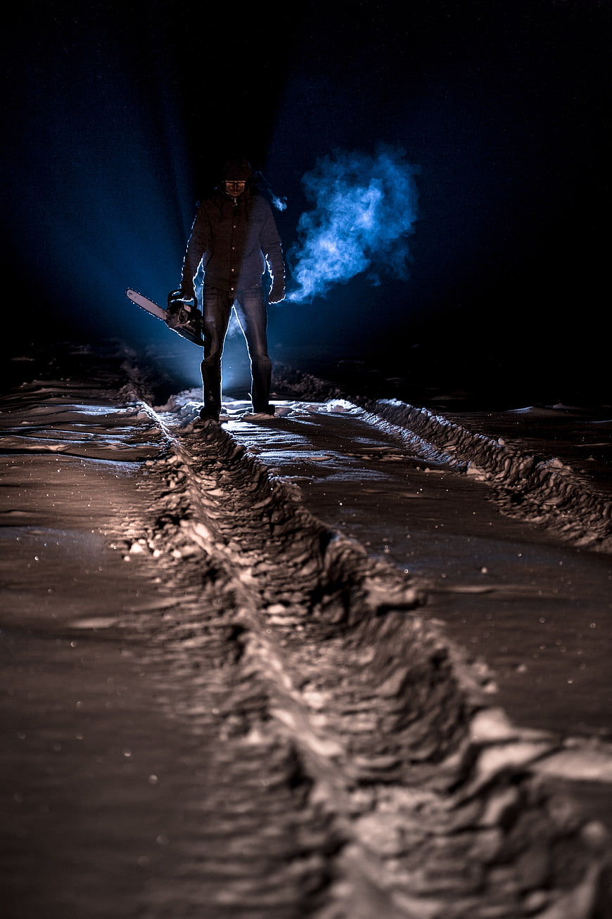 Man with chainsaw in dark snowy forest at night