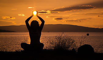 Silhouette of woman holding sun over sea at sunset