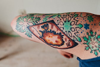 Close-up of colorful snowflake and compass tattoo on arm