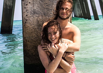 Happy couple hugging under pier in turquoise ocean water