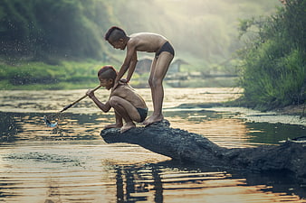 Two boys fishing with a net on a log in a river