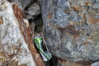 Crushed green soda can wedged between large gray rocks