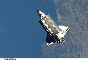 Space Shuttle Atlantis in orbit above Earth's blue ocean and coastline