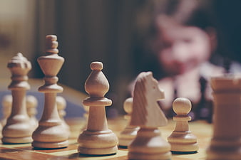 Close-up of wooden chess pieces with blurred player in background