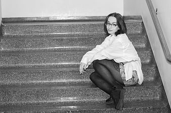 Young woman with glasses sitting on stairs in black and white