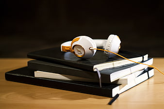 White and gold headphones on stack of black notebooks