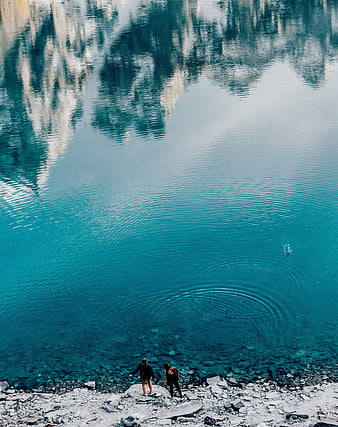 Two people skipping stones in turquoise alpine lake