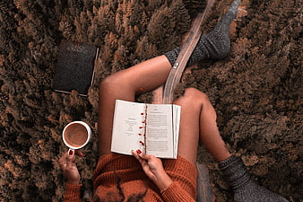 Woman reading book and drinking coffee in autumn forest