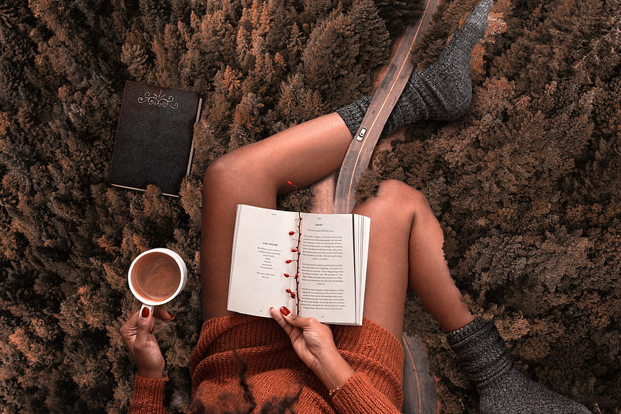 Woman reading book and drinking coffee in autumn forest