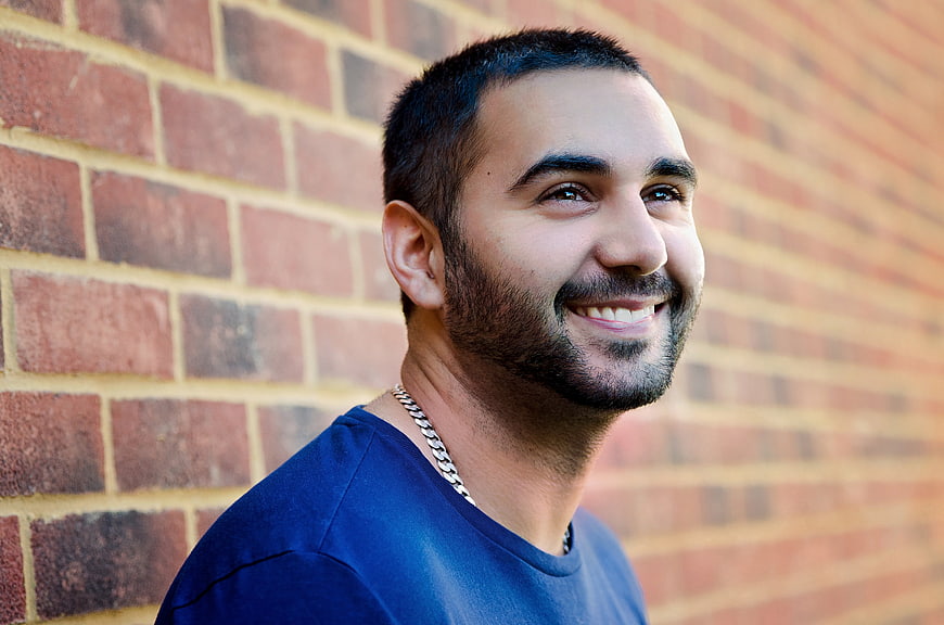 Smiling Young Man In Blue Shirt Against Red Brick Wall