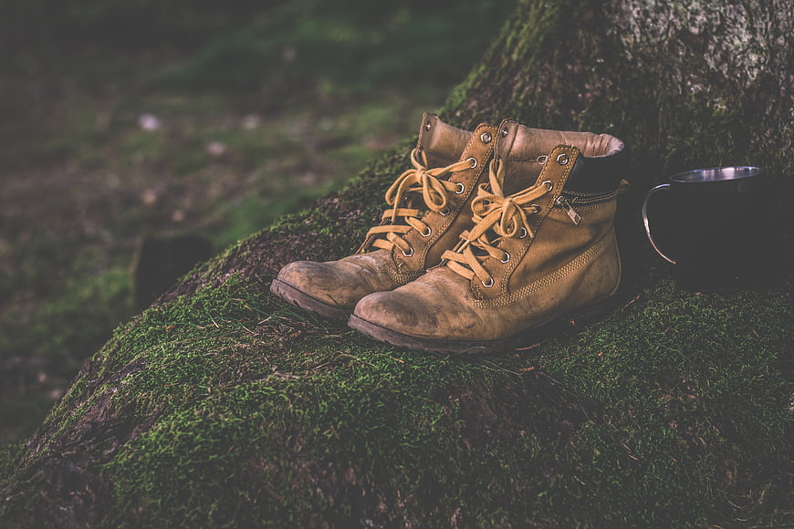 Worn hiking boots and metal mug on mossy log