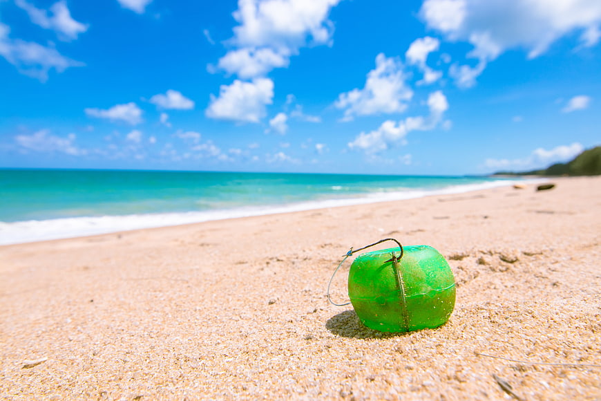 Green plastic fishing float on sandy beach with ocean background