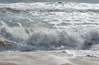 Crashing ocean waves with white foam on sandy beach