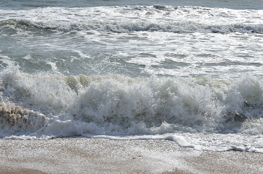 Crashing ocean waves with white foam on sandy beach