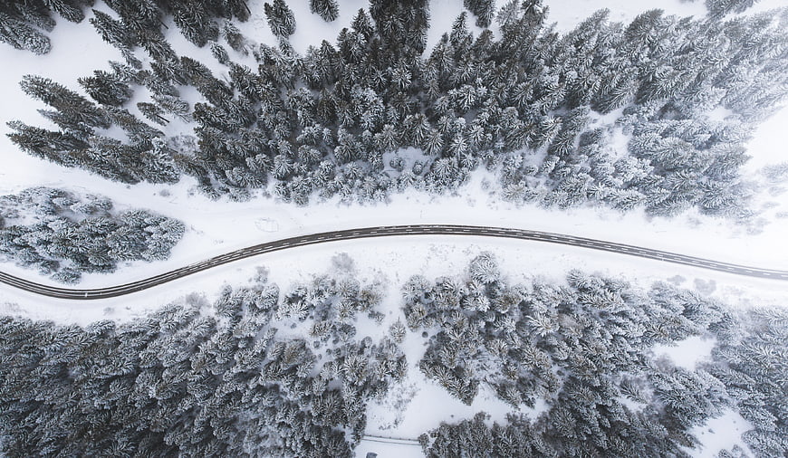 Aerial View of Winding Road Through Snowy Winter Forest