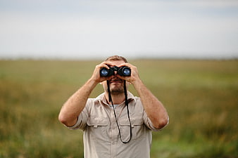 Man with binoculars observing nature in grassy field