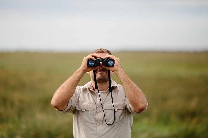 Man with binoculars observing nature in grassy field