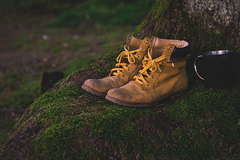 Worn yellow hiking boots and mug on mossy log