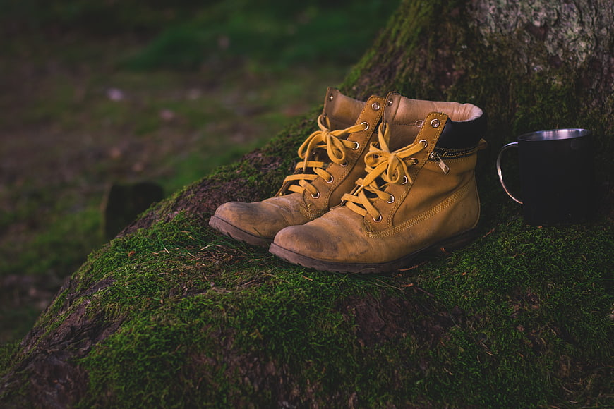 Worn yellow hiking boots and mug on mossy log