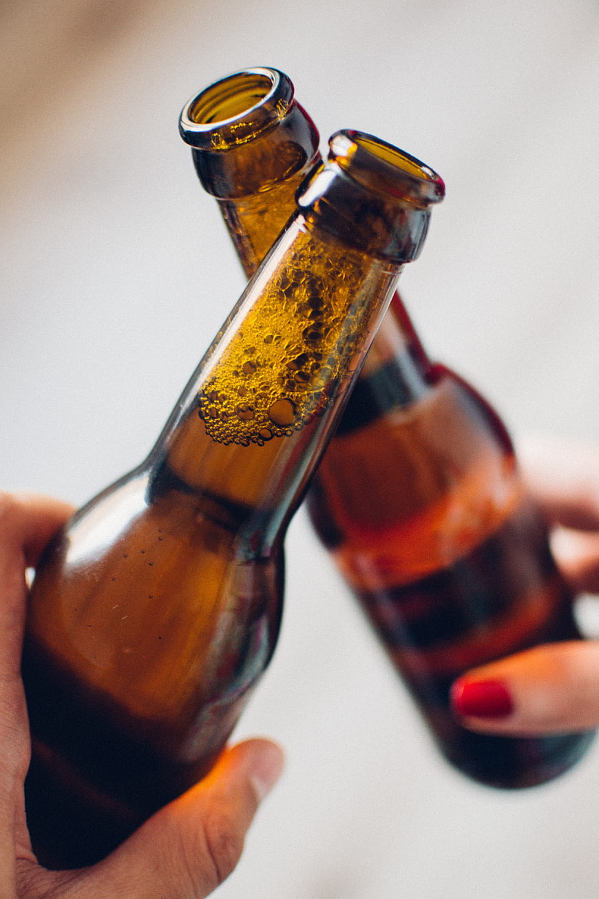 Close-up of two hands clinking amber beer bottles in a toast