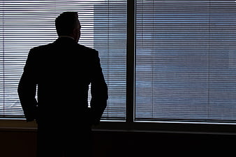 Silhouette of businessman looking out office window blinds