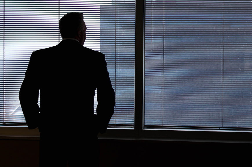 Silhouette of businessman looking out office window blinds