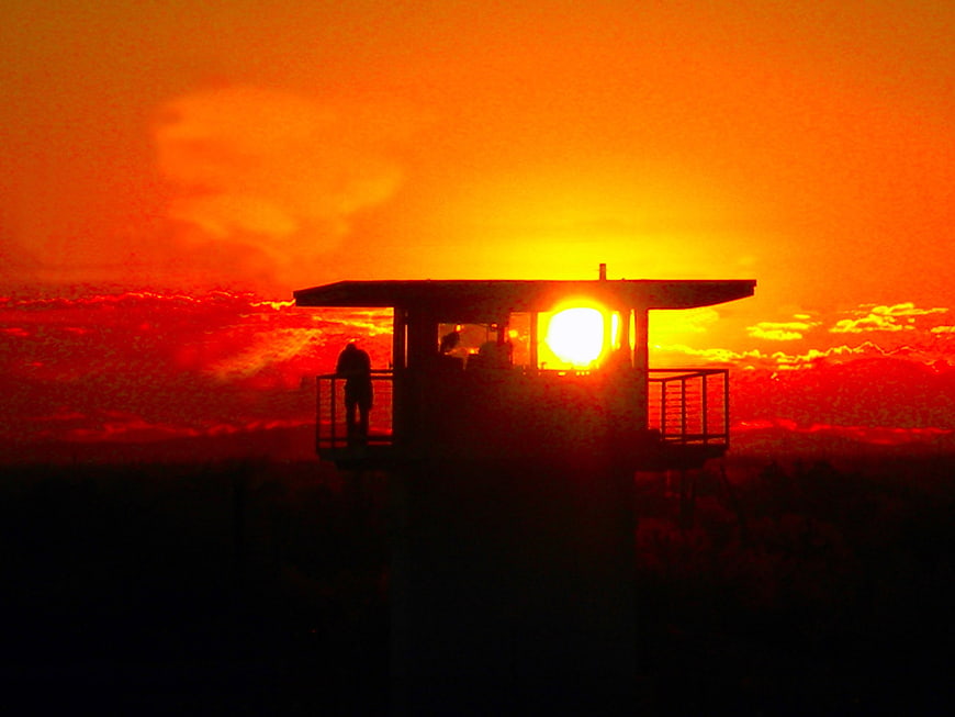Silhouette of a prison guard tower against a fiery red sunset sky