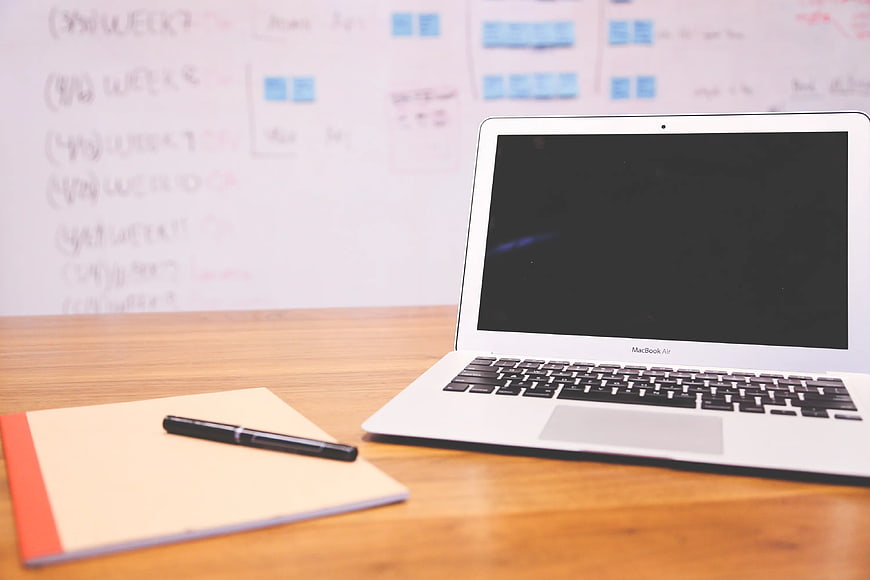 MacBook Air on wooden desk with notebook and pen