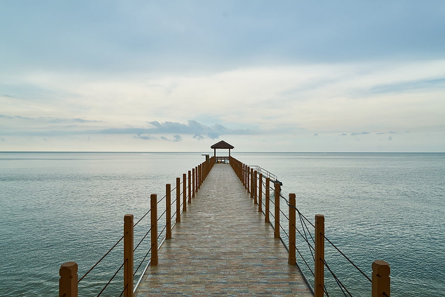 Serene wooden pier extending into calm ocean waters under a cloudy sky