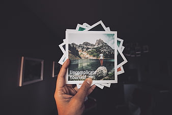 Hand holding stack of photos with inspirational quote Uncomplicate Yourself
