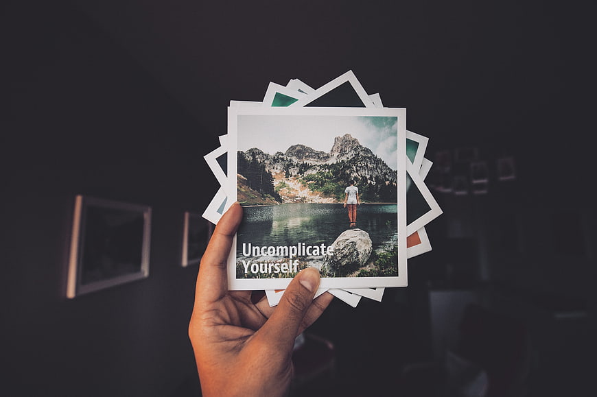 Hand holding stack of photos with inspirational quote Uncomplicate Yourself