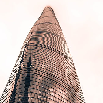 Low angle view of a modern glass skyscraper against a pale sky