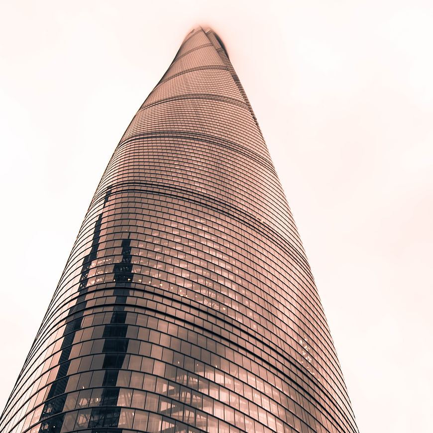 Low angle view of a modern glass skyscraper against a pale sky