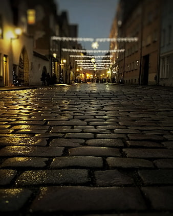 Low angle view of wet cobblestone street with Christmas lights