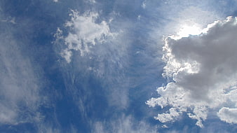 Bright Sun Shining Through Fluffy White Clouds in Blue Sky