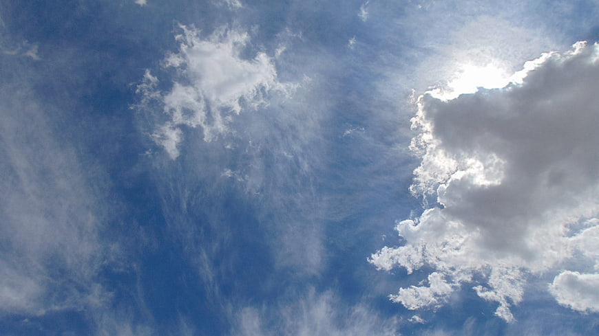 Bright Sun Shining Through Fluffy White Clouds in Blue Sky