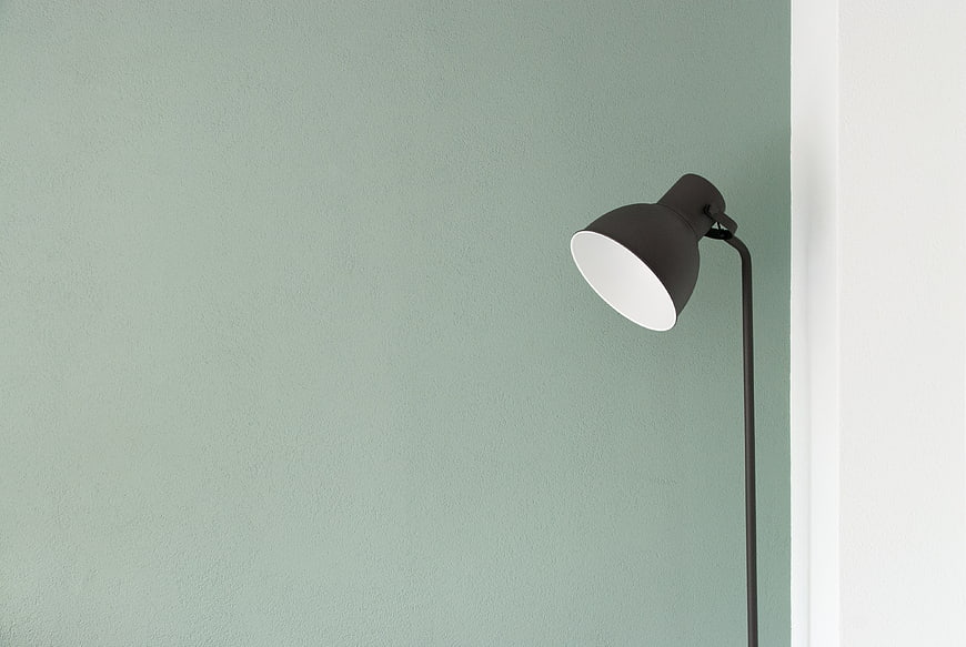 Minimalist black floor lamp against sage green wall