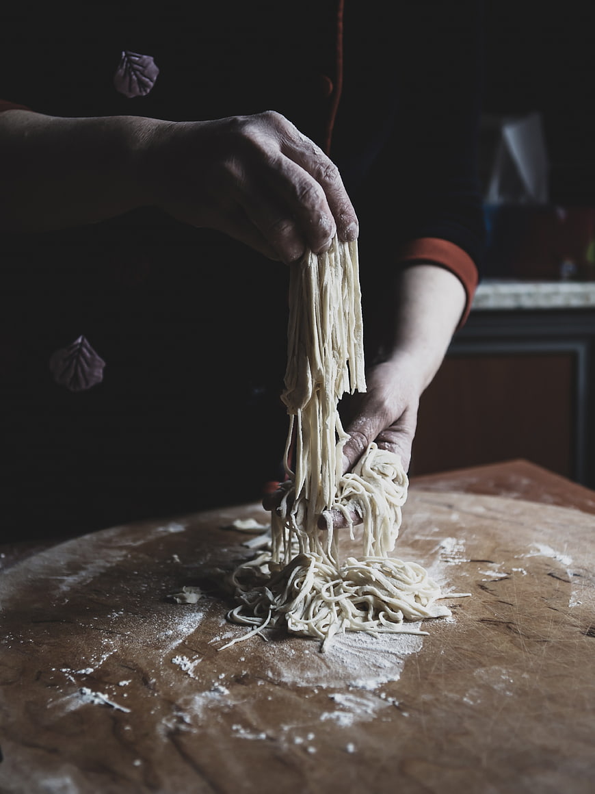 Hands making fresh homemade pasta dough on wooden table