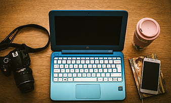 Blue laptop, DSLR camera, and smartphone on wooden desk