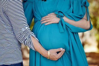 Pregnant woman in teal dress holding belly with partner