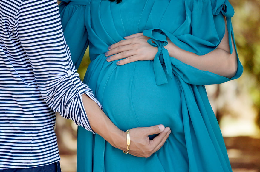 Pregnant woman in teal dress holding belly with partner