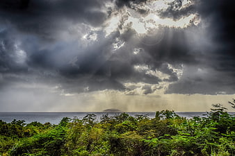 Dramatic storm clouds over ocean with sun rays through jungle