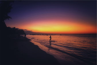 Silhouette of child playing on beach at sunset