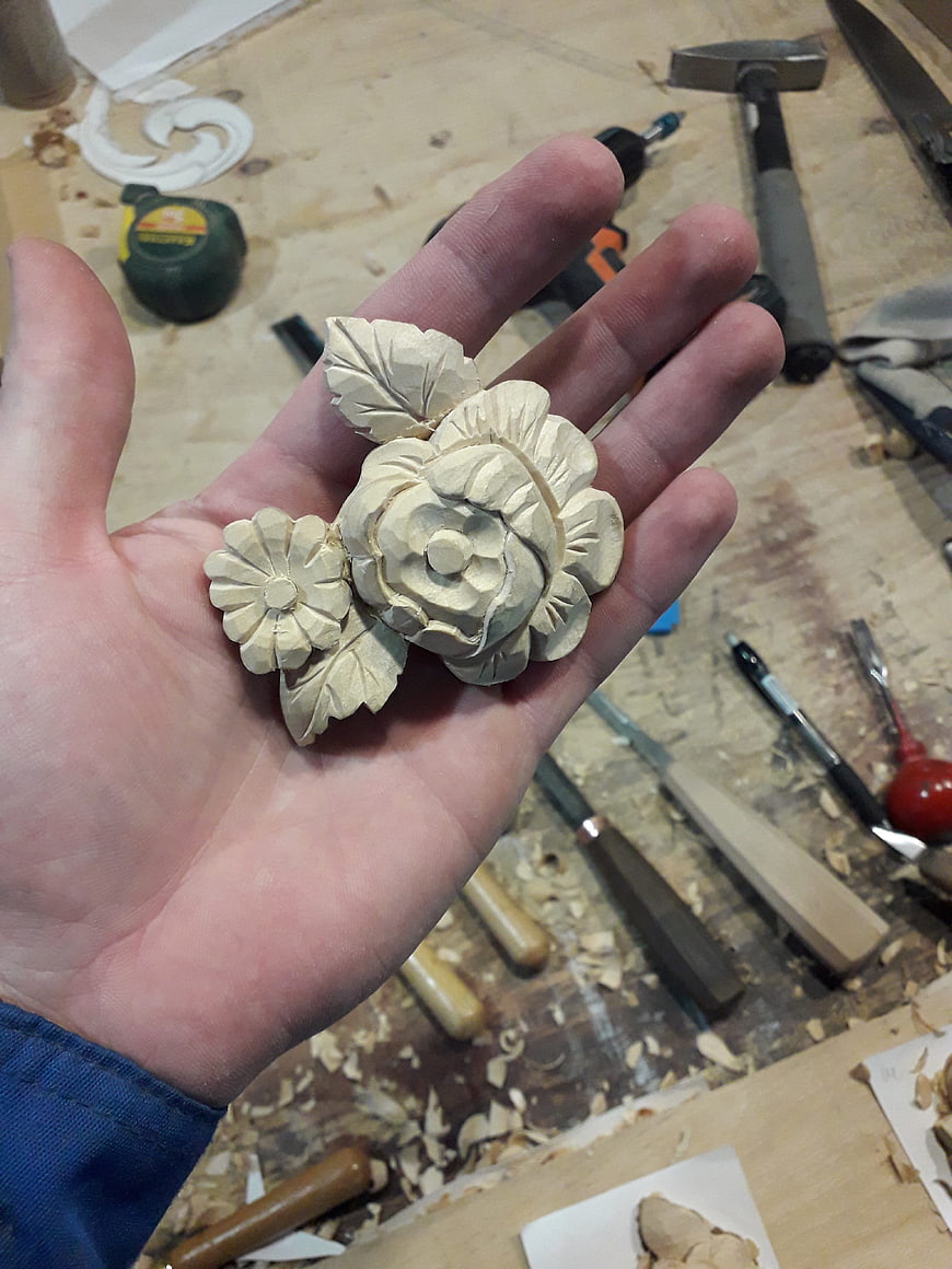 Hand holding carved wooden flowers on workbench