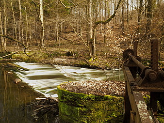 Rusty water wheel mechanism beside a flowing forest stream