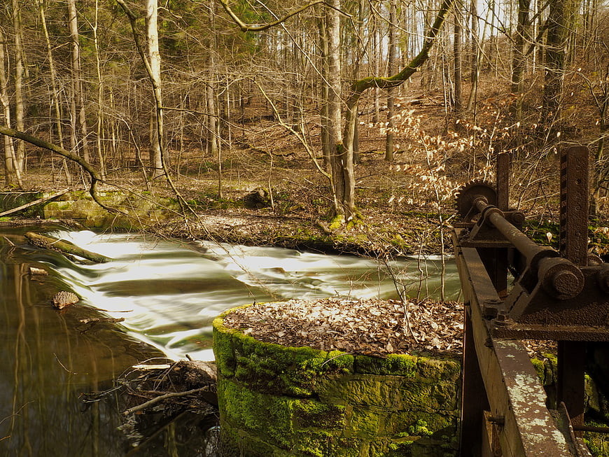 Rusty water wheel mechanism beside a flowing forest stream