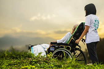 Caregiver pushing elderly patient in wheelchair at sunset