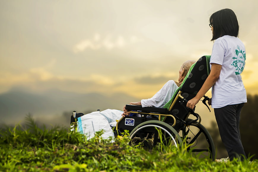 Caregiver pushing elderly patient in wheelchair at sunset