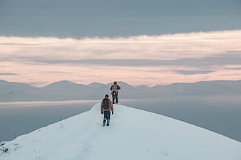 Two hikers walking on snowy mountain ridge at sunset